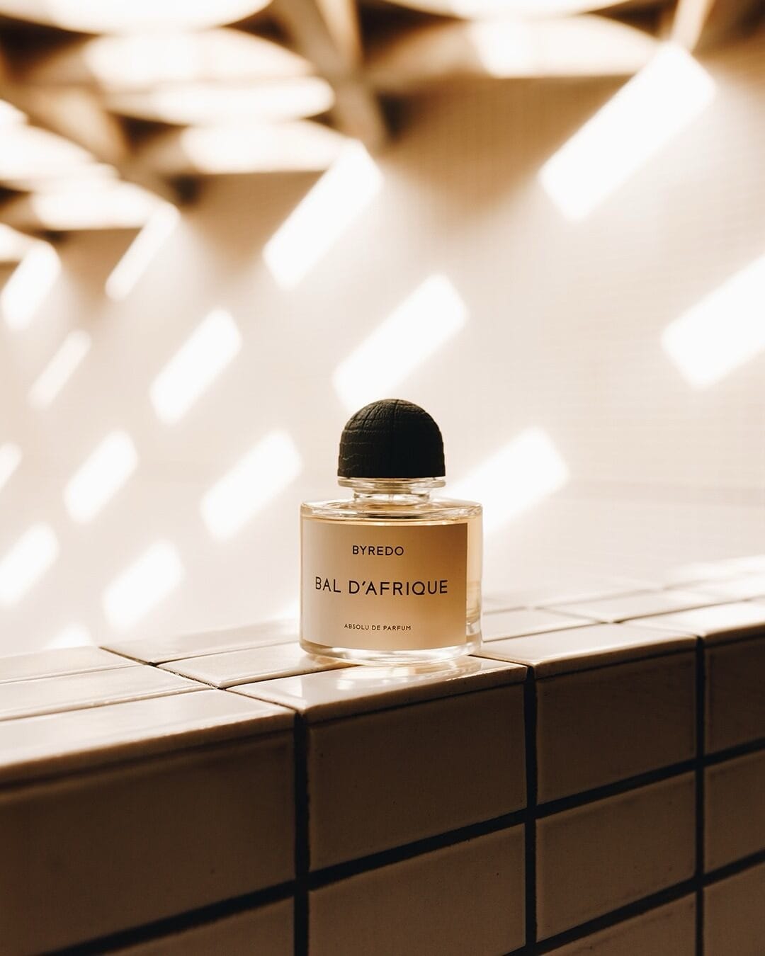 Byredo fragrance product photo: clear glass, matte black cap and pale gold, glass and stone, natural light, image 1 of 3