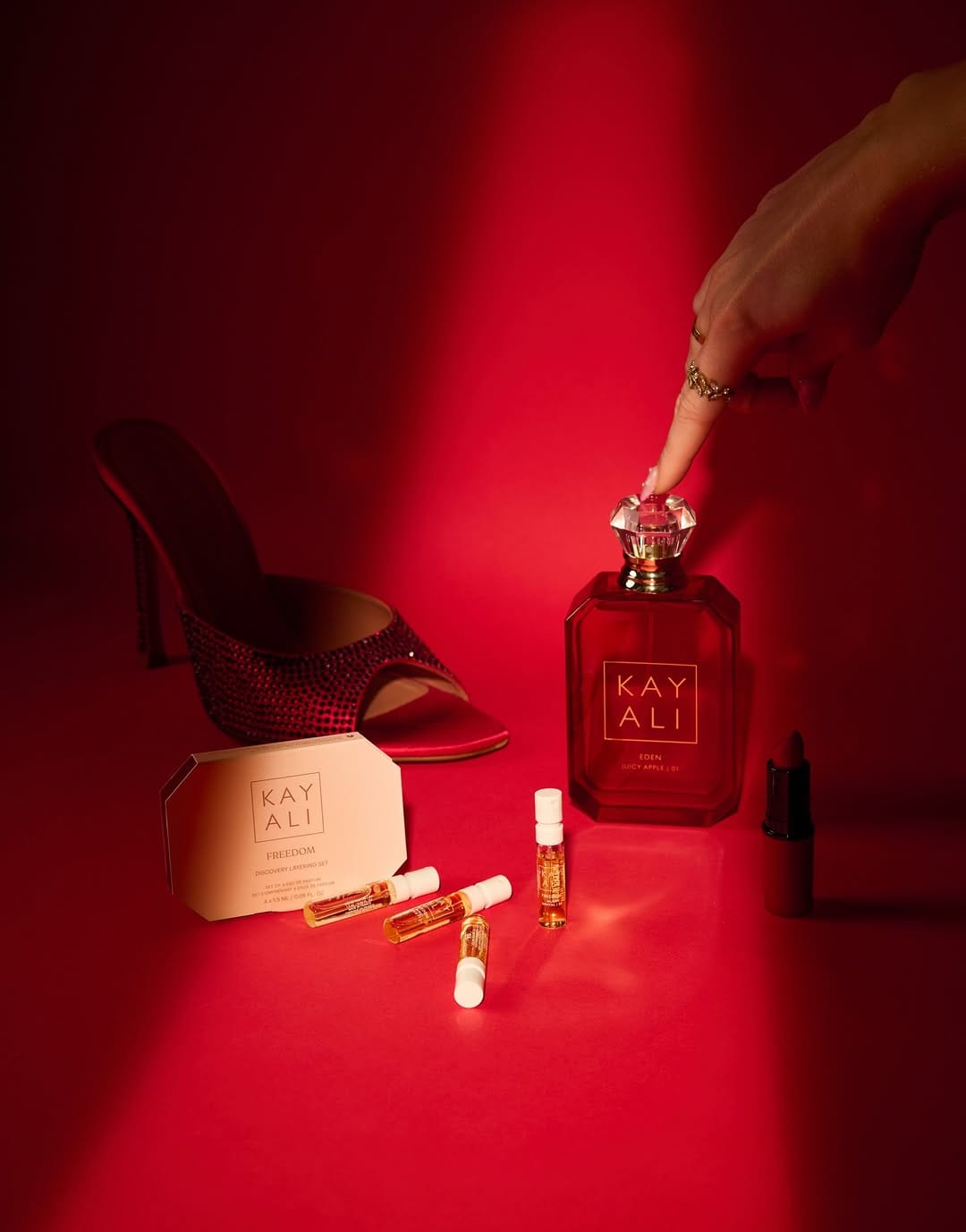 Kayali fragrance product photo: ruby red, peach and rose pink, glass, dramatic light, image 2 of 4