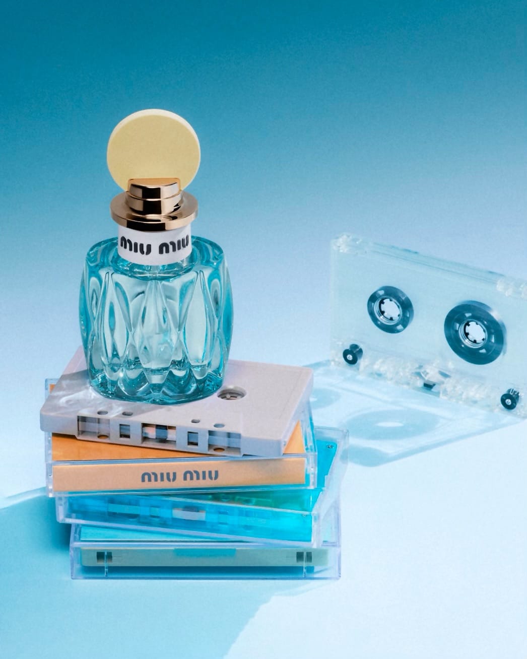 Miu Miu fragrance product photo: aqua blue, peach amber, black cap and gold, glass, soft light, image 1 of 3