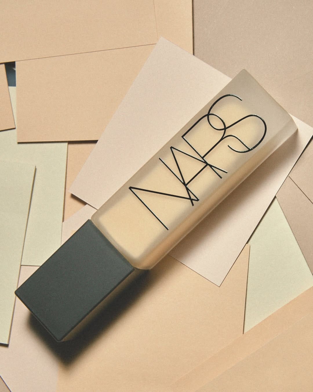 NARS foundation product photo: sand beige and matte black, paper and glass, soft light, image 1 of 2