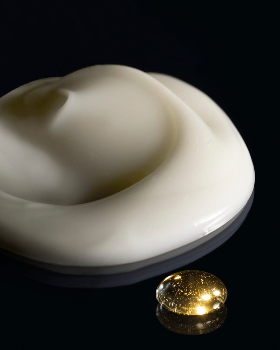 Oribe Gold Lust duo product photo: black glass, amber gold oil and ivory cream, glass, dramatic light, image 2 of 2